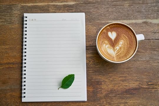 Spiral notebook with green leaf on the page besdie a cup of cappucino with a foam milk heart