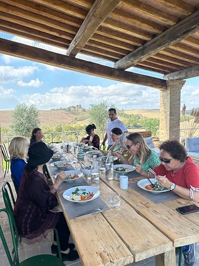 Image shows a trestle table outside with people eating lunch. 