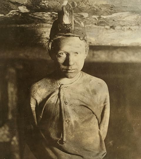 A preteen boy with a grimy face and filthy shirt faces the camera, deep inside a coal mine.