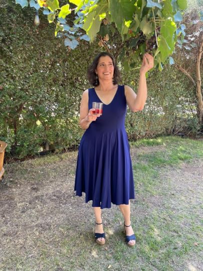 Black haired woman in a blue dress picking a grape from a vine.