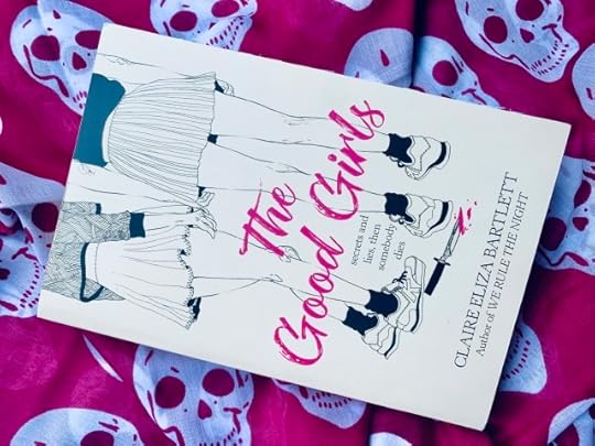 THE GOOD GIRLS (with cover art depicting the legs and feet of a group of young women standing together) against a backdrop of skulls. Hot pink appears on the book cover and in the background. Photo by AHS.