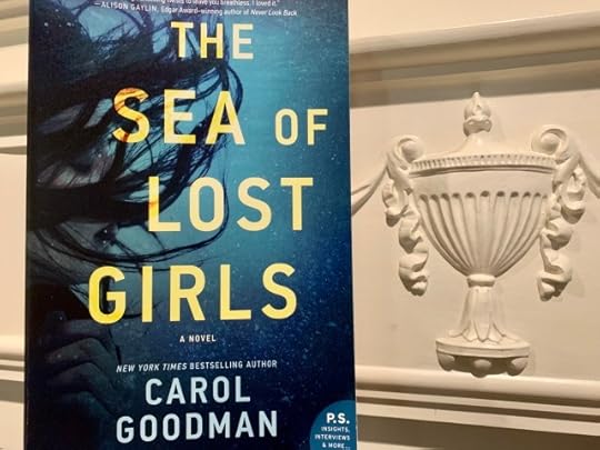 Shown is THE SEA OF LOST GIRLS (with cover art depicting a woman's face under water) beside a carving of an urn. Photo by AHS.