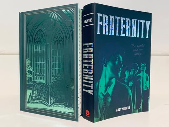 Shown is the Unplugged Book Box special edition of FRATERNITY. The naked hardback has a foiled pattern of an open tome underneath a Gothic window. The book cover has artwork depicting four young men who are classmates. Both have green and black colors. Photo by AHS.