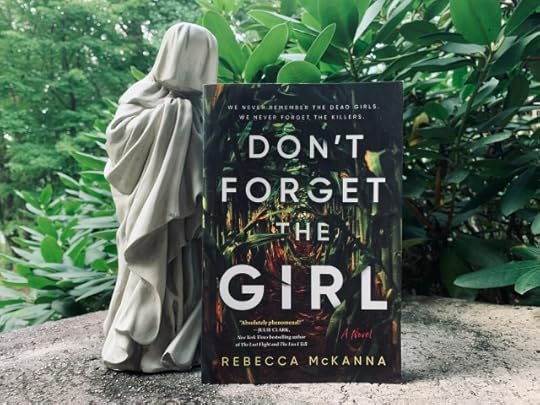 Shown is DON'T FORGET THE GIRL (with cover art depicting a corn field) against a backdrop of greenery, with a veiled weeper or pleurant beside the book. Photo by AHS.
