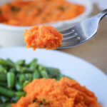 scoop of sweet potatoes on a fork above a plate of food.