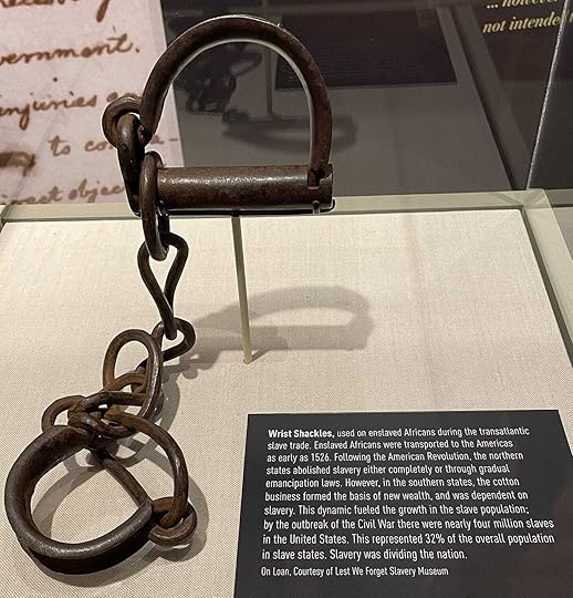 Iron wrist shackles in display case with accompanying museum label.