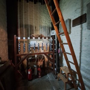 view of tubular bells tucked behind red curtain to vestry at St Andrew's Leighterton
