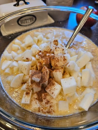 A glass mixing bowl with baked apple oatmeal batter, with a sprinkle of cinnamon on top