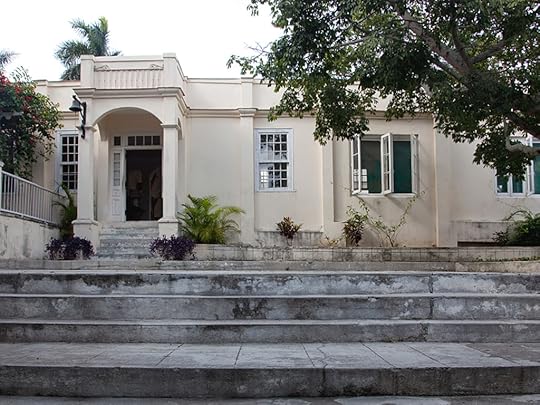 A one-story, flat-topped stucco home, with very wide concrete steps leading up to the level of the house. The house is beige with several wiindow and an arched awneing over the front door.