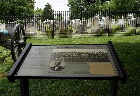 Color photo of an explanatory marker, including two photos of Lincoln, just steps away from a graveyard behind a black metal fence. A cannon stands at left.