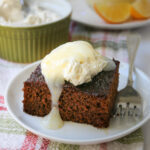 square of gingerbread on a plate with a fork, the cake is topped with cream cheese and lemon sauce.
