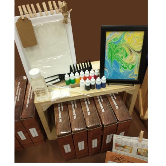 Photo of Water Marbling Crate showing Example Water Marbling Project in a frame, paints, comb tool, thickener, tube tools, tray, paper, tag, clothespins, jute string and crates sitting on a wooden box