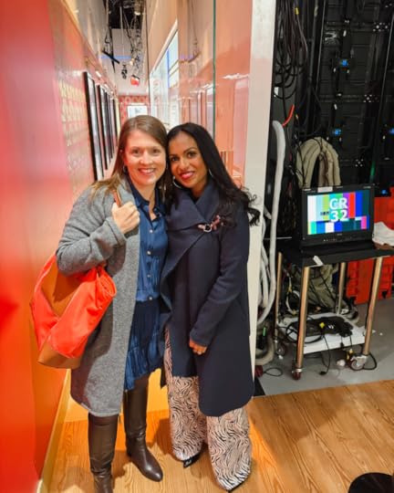 Amy Julia and Niro wear coats and stand inside NBC studios as they smile at the camera