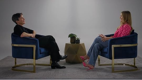 Cillian Murphy in black and Margot Robbie in a pink coat sit opposite each other in chairs