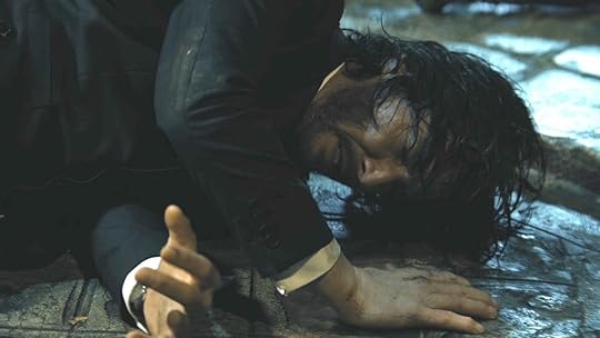John Wick wearing a dark suit in agony on the ground near stairs in John Wick: Chapter 4, one of the best TV and movie moments of 2023 according to Nerdist