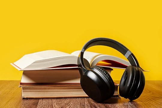 A stack of books, the top one open, with a pair of headphones resting against them.