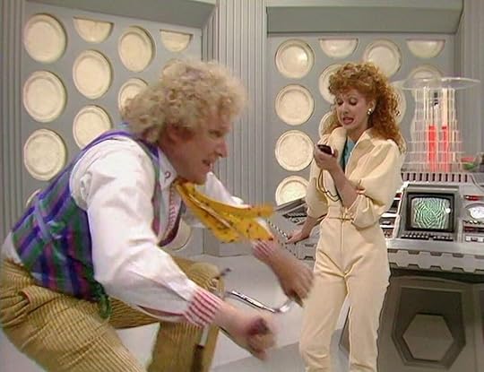 Mel (Bonnie Langford) holds a stopwatch while the Doctor (Colin Baker) rides a stationary bike in Doctor Who.