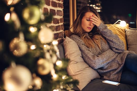 Women sitting beside Christmas tree and looking tired or depressed.