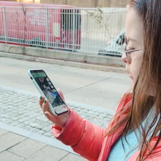 side profile of Penny standing on a sidewalk looking at her phone that is open to google maps