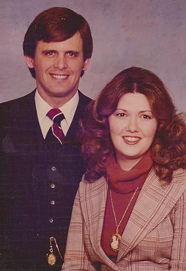 A man in a dark suit with his wife wearing a red suit