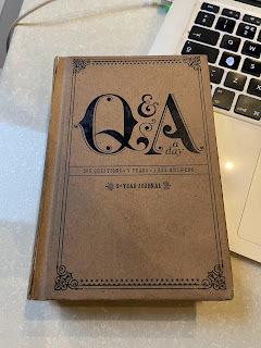 A small, light brown notebook. On the front, in large black letters, it says, 'Q and A a Day.' Underneath in smaller letters, it says, '365 Questions * Five Years * 1825 Answers'. Underneath that, it says, '5 Year Journal.'