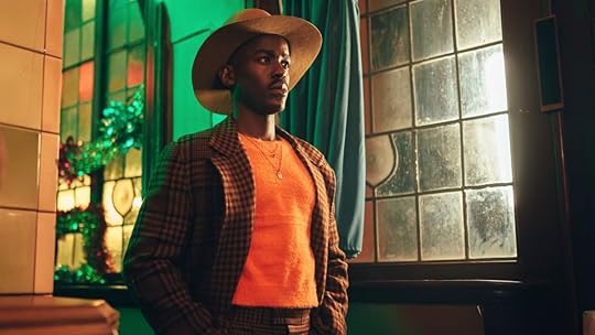 Ncuti Gatwa as the Doctor stands near a glass stained window wearing a checkered brown suit, orange sweater, and a cowboy hat