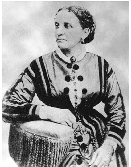 Black and white photo of a well dress woman seated, her right forearm rested on the cushioned edge of a couch, looking to her right.
