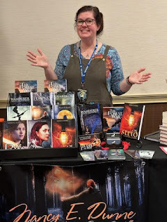 A woman stands behind a table full of books for sale.