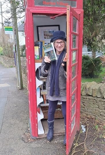 Debbie holding a book in the door of a Little Free Library