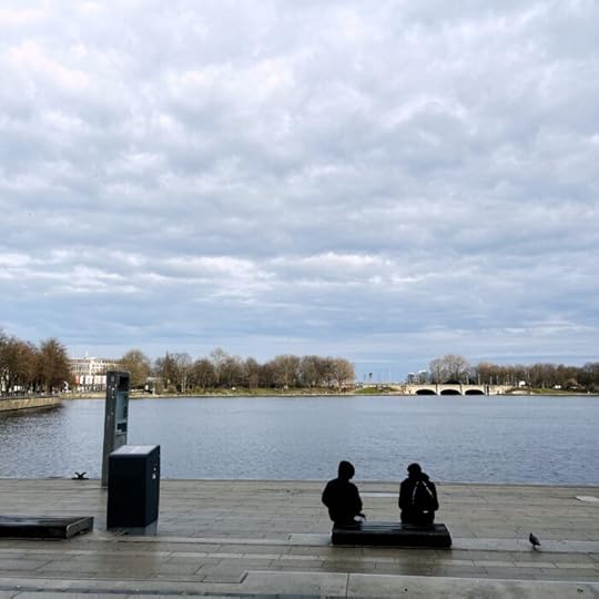 Zwei Menschen (von hinten gesehen) sitzen auf einer Bank am Jungfernstieg und sehen auf die Binnenalster.