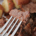 a bite of pot roast on a fork with meat and potatoes in the background.
