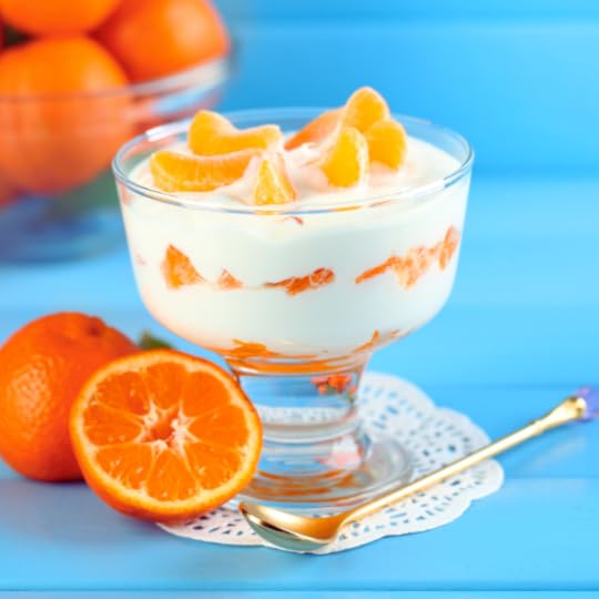 White custard layered with oranges in a glass compote bowl surrounded by orange slices