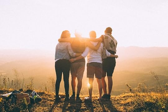 Four friends standing together, watching a sunset over a mountainous landscape, with arms around each other.