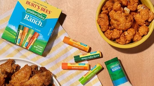 Food-flavored lip balms surrounded by Buffalo sauce, chicken, Hidden Valley ranch dressing on a table