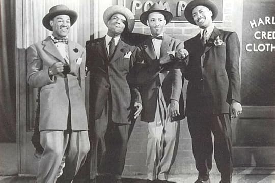 Four men in suit, ties and hats, smiling at the camera in what looks to be a television or radio studio