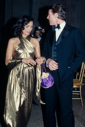 Bianca Jagger wearing a golden close-fitting gown, with crossed neck straps and bare shoulders