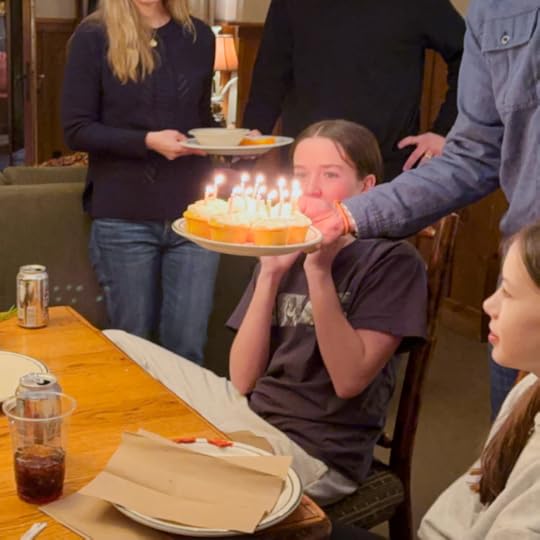 a plate full of lemon cupcakes (each one has a candle) is being lowered to the table in front of the birthday teenager