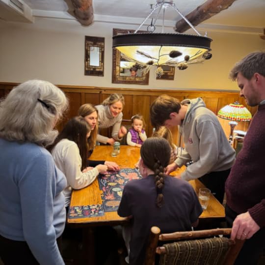 three generations of a family lean over a table putting together a puzzle