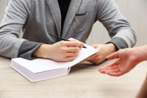 Author signing autograph in own book at wooden table on white planks background