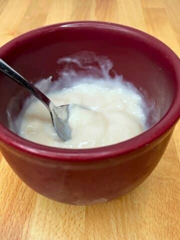 Dairy free pudding mix is in a red bowl with a metal spoon. Ready to serve and enjoy.