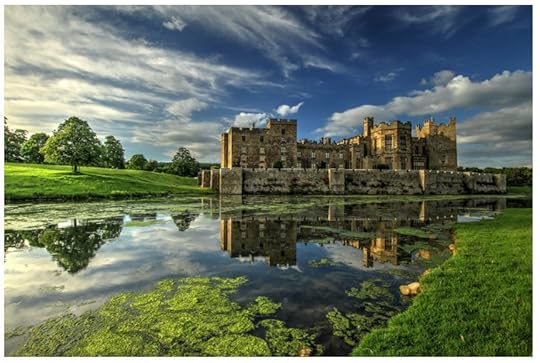 Long shot of medieval castle with long battlements across the front and protective walled walkways. The castle is set against lush parklands on one side and a tranquil lake on the other.