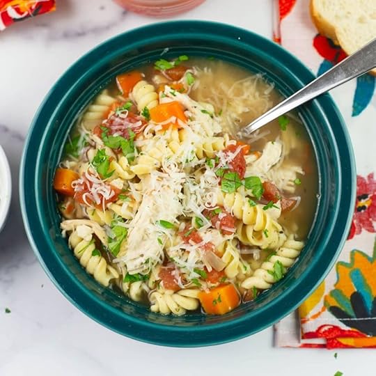 Closeup image of Italian Chicken Noodle soup served in a dark teal bowl with a spoon.