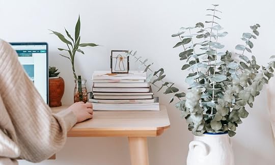 female working on a laptop at a desk, stack of books on the desk; what is a manuscript review?