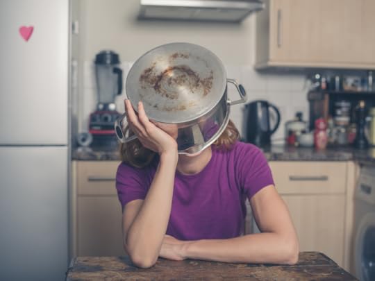 A young woman sits in her kitchen, with her head in a big saucepan