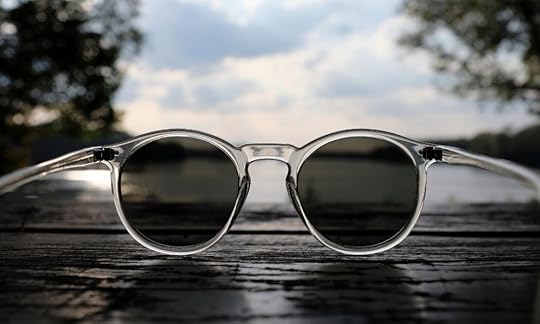 sunglasses resting on a table with a lake and sky in the background; third person point of view