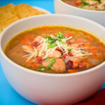 close up of bean soup in a white bowl on a teal tray.