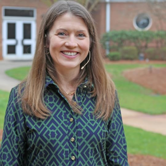 Amy Julia smiles at the camera. She is wearing a green dress and standing in front of a church. She has on a wireless mic.
