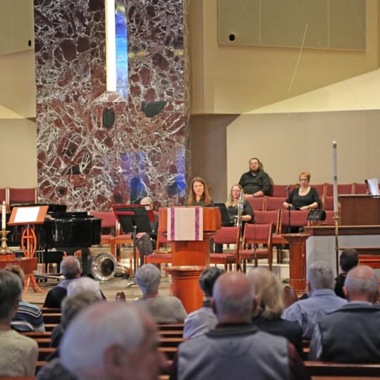 Amy Julia stands behind a pulpit inside a church sanctuary. People are seated and listening to her.