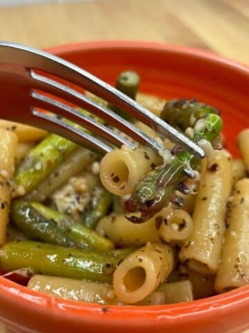 Orange bowl with fork Asparagus Pasta recipe on brown table background.