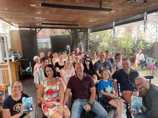 Book launch of fantasy book Origin Curse by Sarah Kate Ishii, with an audience smiling at the camera and holding up books.